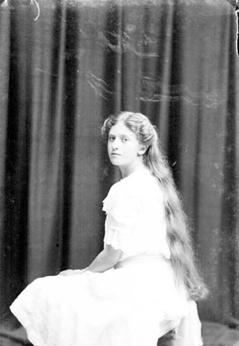 Porträtt av en sittande flicka med långt hår i en ljus klänning.