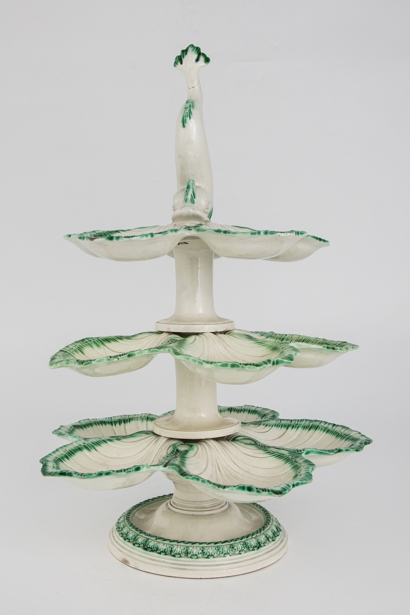 Bordoppsats/ etasjefat med palmetter, østersformede skåler og plastisk delfinfigur. Østersskålene er grønnglasert med en fjærrand.