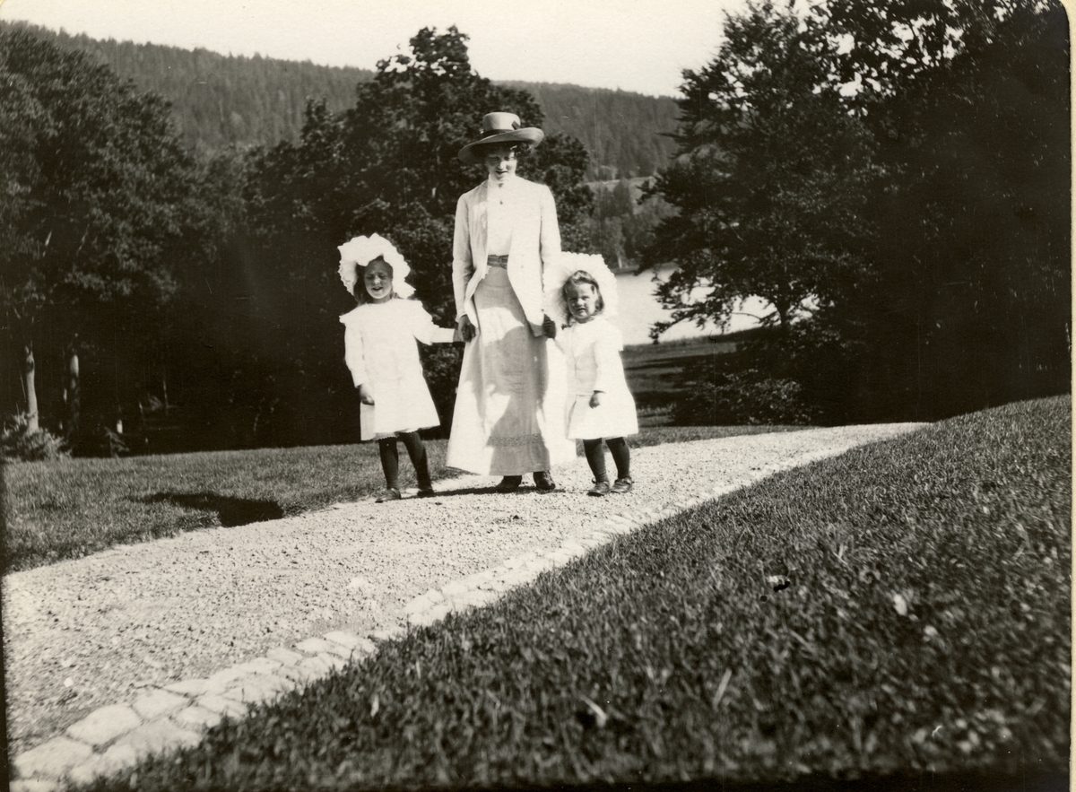 Søstrene Mimi og Lucy Egeberg går tur i parken på Bogstad gård med frk. Knudsen (barnepike?). Fotografert juli 1910.