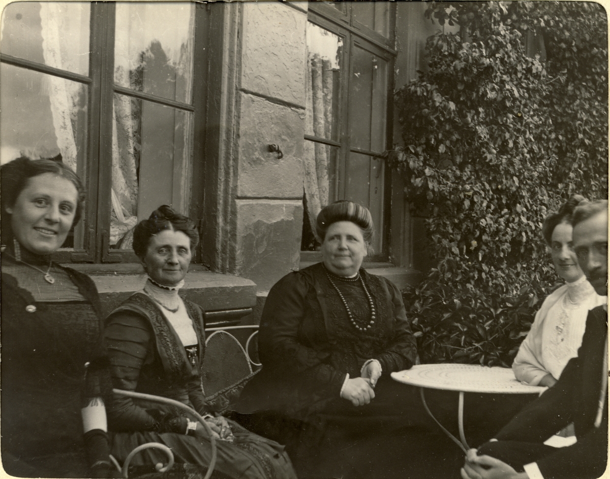 Fire kvinner og en mann på verandaen til Bogstad gård. Fra venstre Anna Astrup, Mimi Wedel Jarlsberg, Edle Wedel Jarlsberg, Nini Egeberg og Edle Wedel Jarlsberg svigersønn, Antonio Borgiano. Fotografert august 1911.