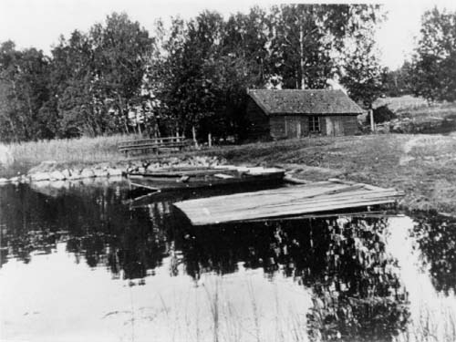 strandparti-vid-aran-s-g-rd-en-liten-stuga-och-en-eka-som-ligger-vid