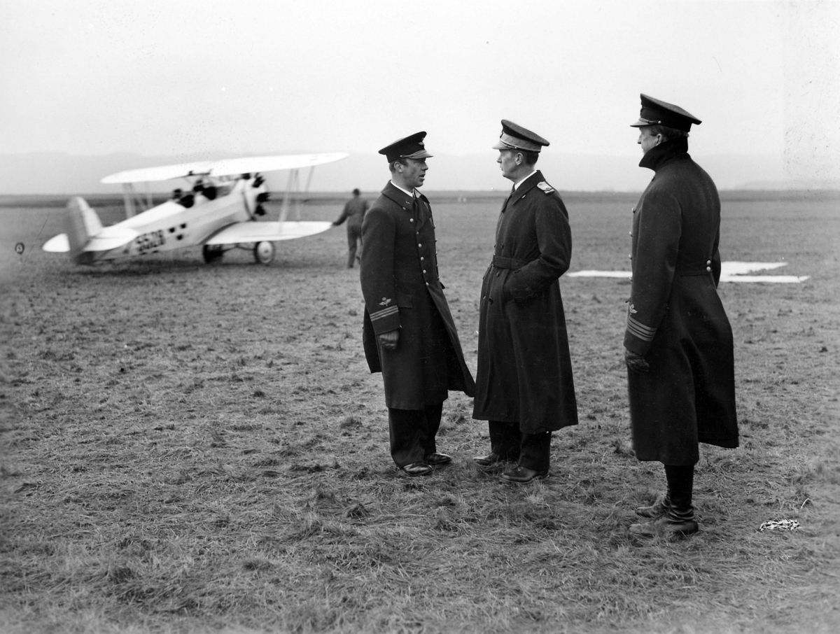Tre militärer ur flygvapnet står på ett flygfält. Från vänster Nils Söderberg, Torsten Friis samt okänd. I bakgrunden står flygplan Sk 10. Cirka 1932-1939.