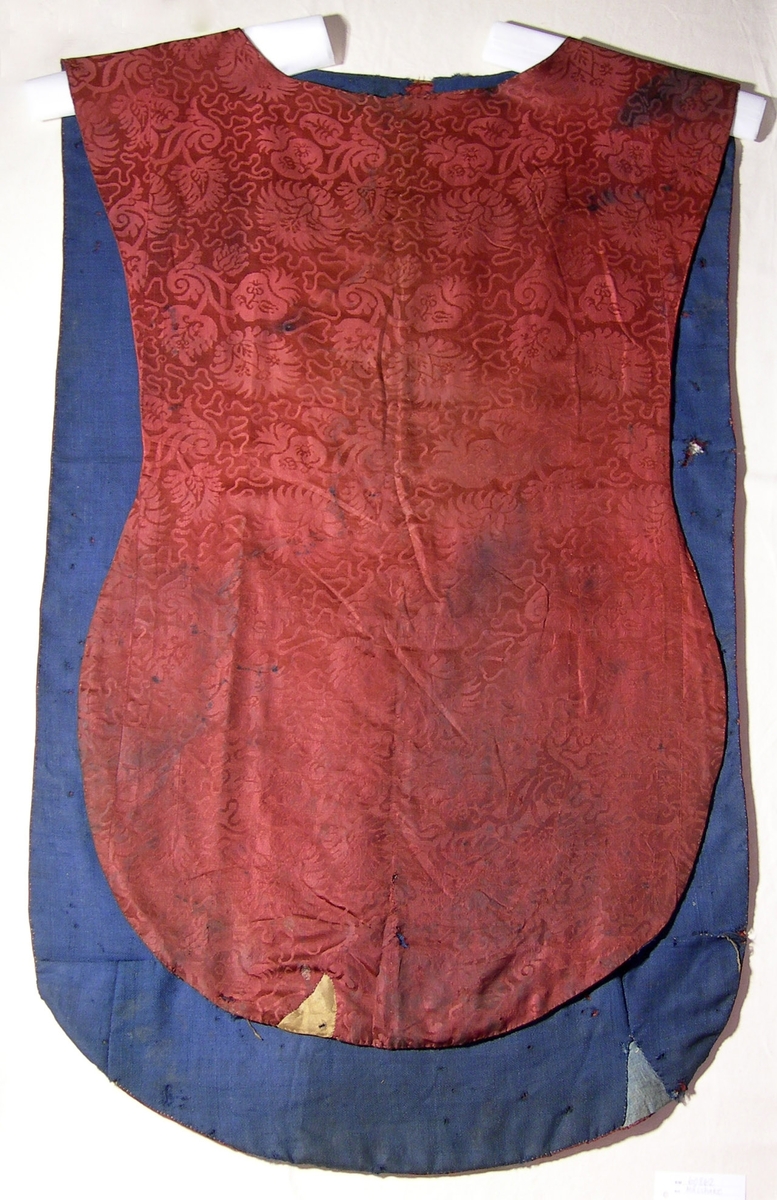 Sidendamast i 5-skaftad satin, röd.
Varp: rött silke, ca 40 tr/cm
Inslag: rött silke, ca 26 tr/cm
Blad- och blommönster omgivet av mjuk slinga.
Yllefoder i liksidig kypert (2/2), blått. Fodret lagat på några ställen med blått linnetyg, tuskaft.
Mässhaken har axelsöm och är sydd av flera stycken.
På baksidan 695 x 420 mm högt applicerat kors av 2 spetsar i metalltråd (spunnet lan, silver; lan, silver), tillsammmans 30 mm breda.