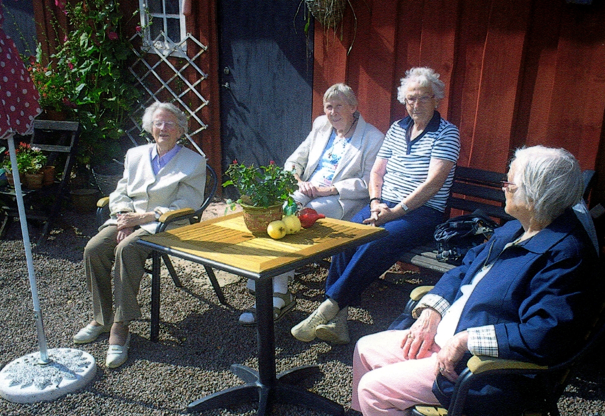 "Göteborgs studiecirkel" är på utflykt och fyra kvinnor sitter och fikar utanför Vommedal Östergård 2:90 "Olas", 1990-tal. Från vänster: Maj-Britt Björkman, Greta Nilsson och Asta Carlsson. Okänd kvinna till höger. Relaterat motiv: A2942.