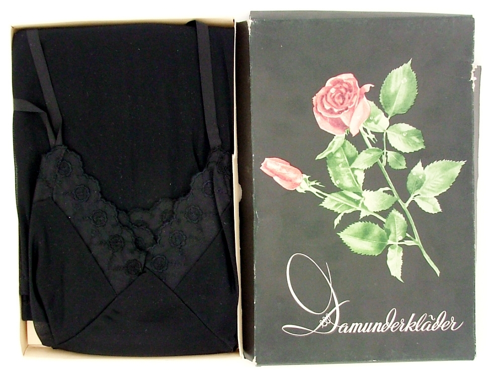 Svart underklänning i originalförpackning med texten Damunderkläder.
Svart botten och ros på förpackningen.