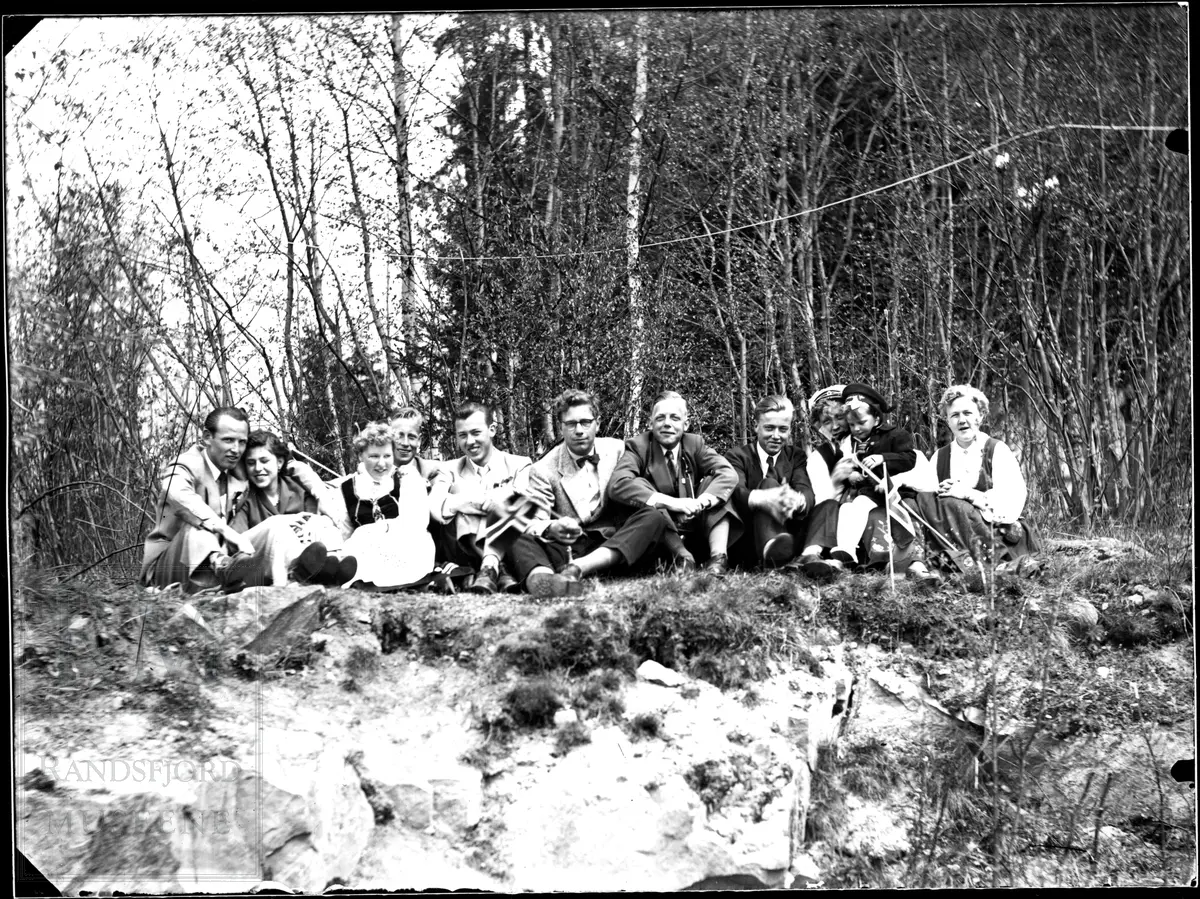 En gruppe på 11, 6 menn, 4 kvinner og et lite barn samlet oppe på en knaus foran noen løvtrær.