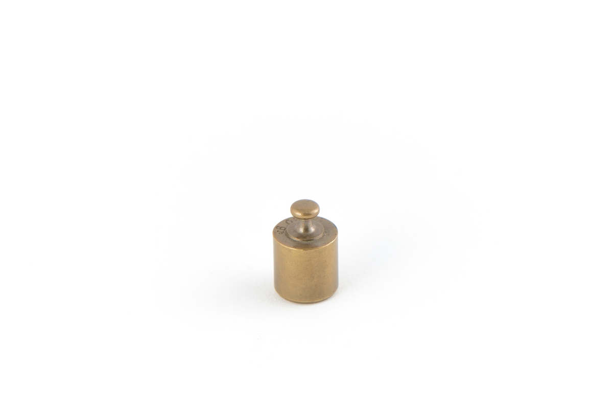 Cylinderformad vikt av mässing, knopp upptill och med flat botten.