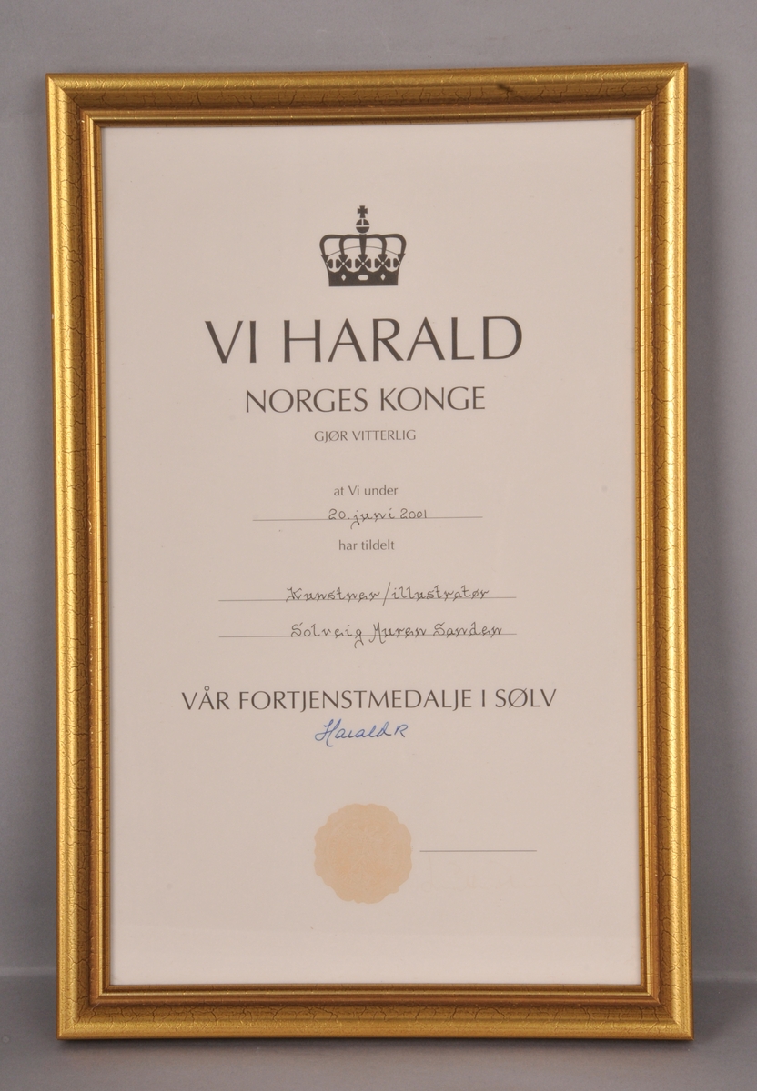 Diplom i glas og ramme. Kongens fortjenestemedalje i sylv, tildela Solveig Muren Sanden i 2001. Gullfarga treramme.