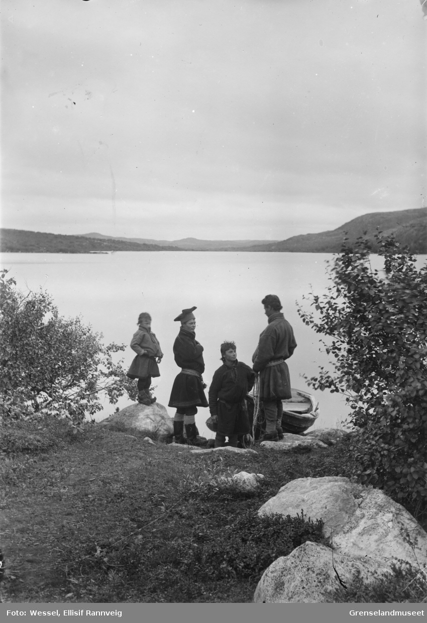 En robåt i vannkanten ved Førstevannet, Kirkenes. Utsikt sørover. Fire unge gutter står på land. Fra venstre på en stein Mattis Pak, Samuel ? med stjernelue, Ole Pak og Jon Pak.