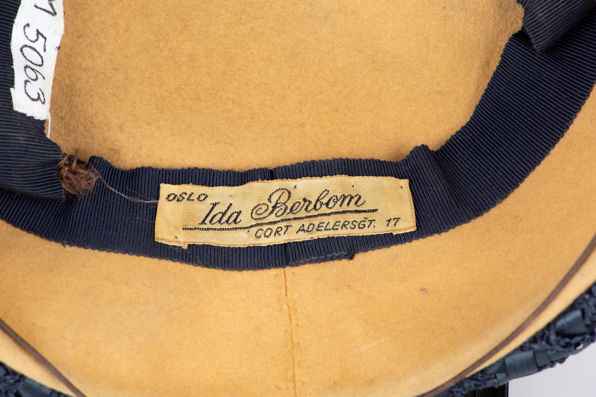 Flat liten hatt med kant av blå tråd og og bast.
Brukt av Olga Ambjørnrud under 2. verdenskrig