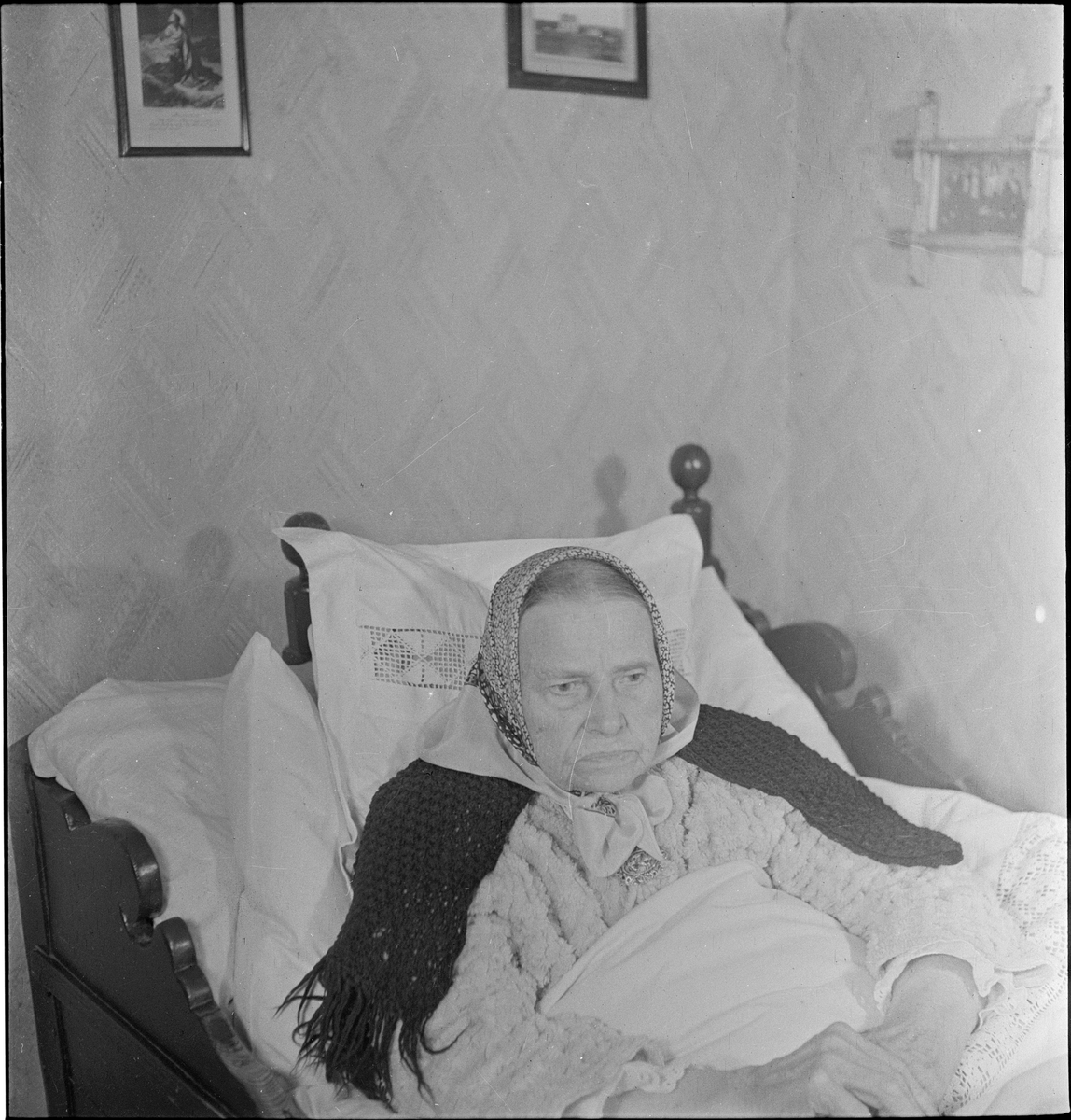 En kvinne sitter ved siden av en eldre sengeliggende kvinne.