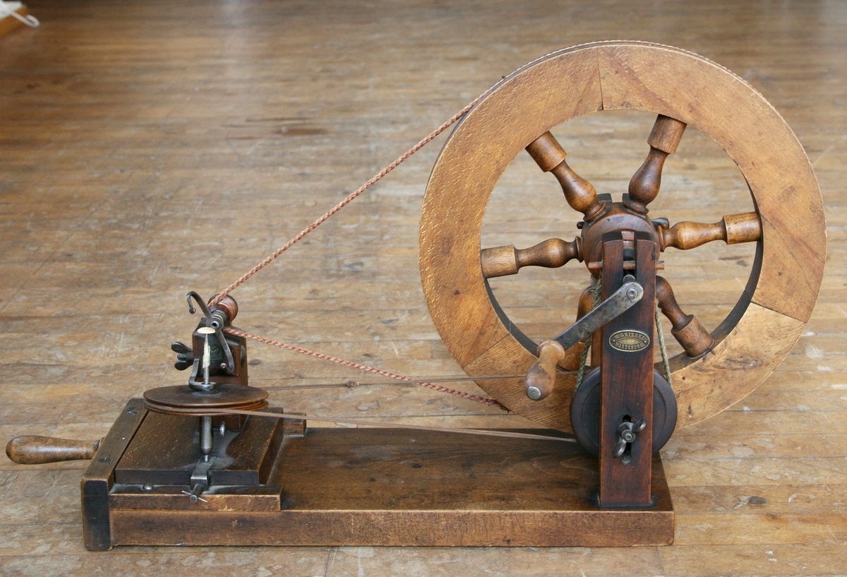 Maskinen är byggd på en träplatta. På plattan ett handvevat hjul som genom ett snöre driver en bygel som lindar garnet runt knappen. Knappen roterar runt. Märkt: M. GRIEBEL MAGDEBURG

Funktion: Lindning av trådknappar