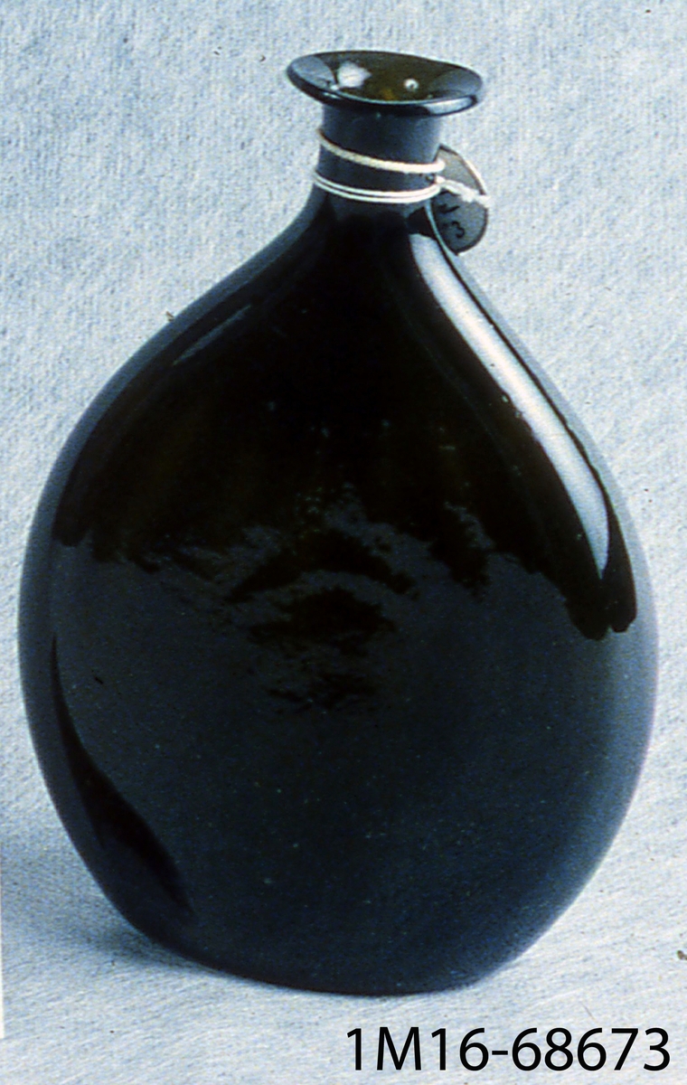 Flaska av mörkbrunt glas, tillplattat rund, med avsmalnande hals.