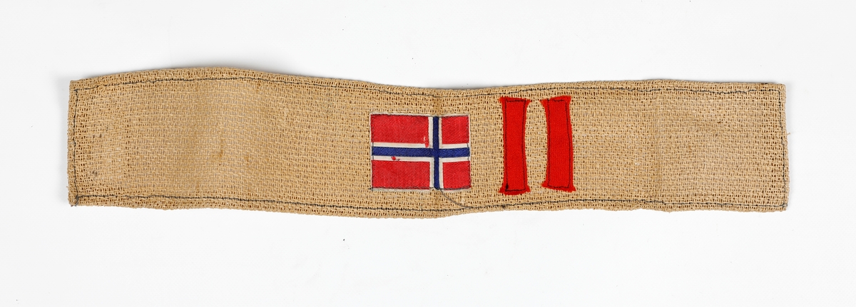 Armbind laget av vevd papir. Norske flagg og to røde bånd sydd på.