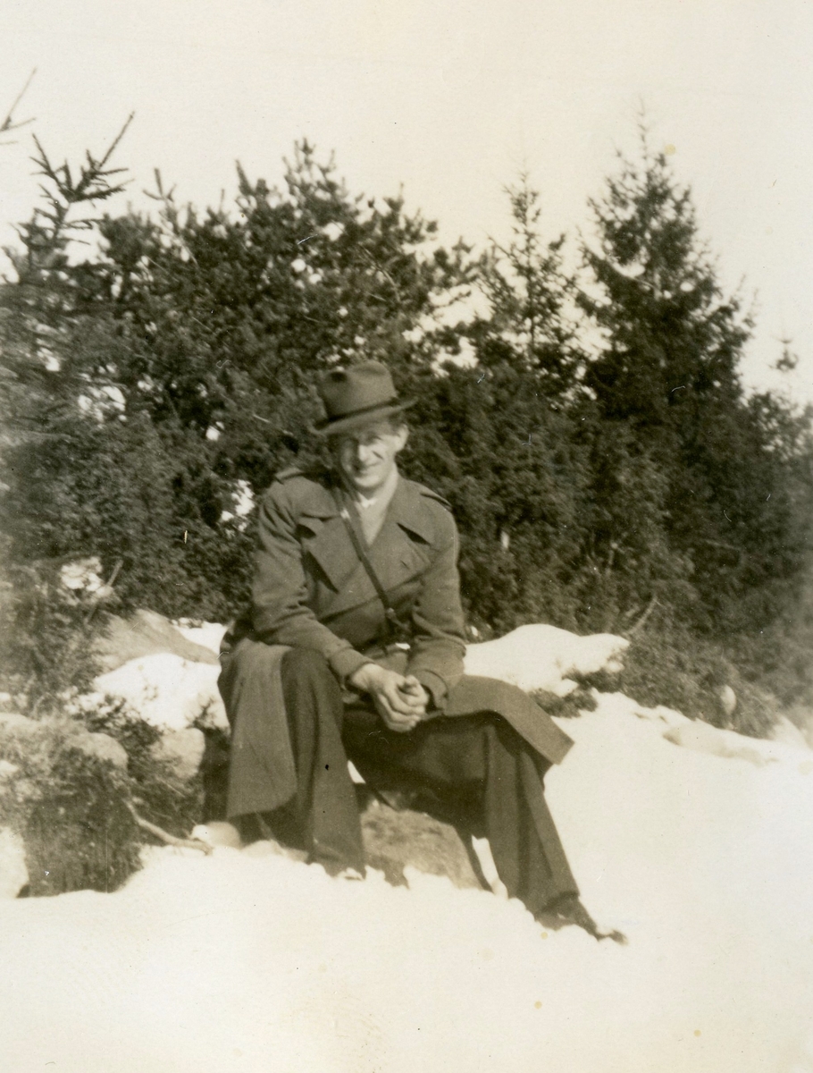 Björn Ekman (1913 - 1992) sitter på en sten i ett snörikt landskap, "Rothvalls" Vommedal Östergård tidigt 1940-tal. Familjen bodde vid "Rothvalls" på Streteredsvägen 31.