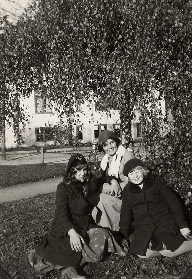 En kvinna har satt sig med två flickor i en trädgård.