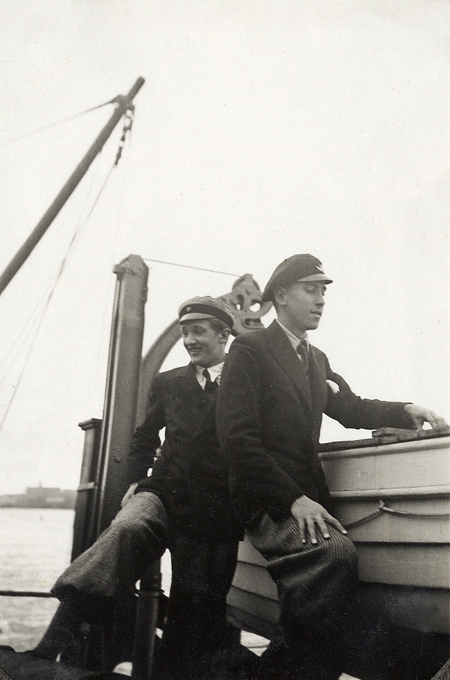 Två unga män i kavaj och skolmössa poserar vid en livbåt.
