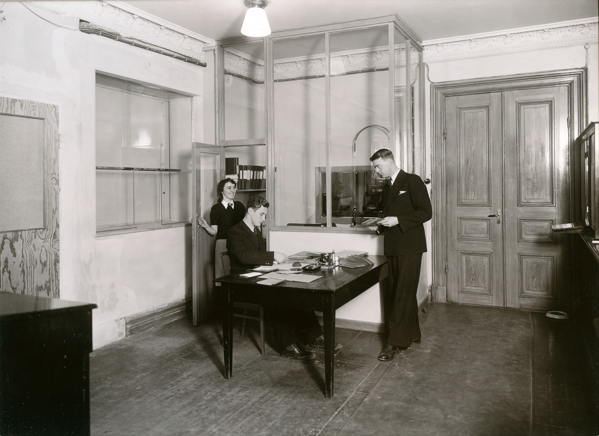 Kontoret på Alingsås Bomullsväveri, gamla fabriken vid Södra Strömgatan. Bilden tagen 1942 före ombyggnaden av kontorslokalerna. Från vänster: Ulla Karlsson (telefonist), Stenholm (kontorist) och Alf Nyström (kontorist).