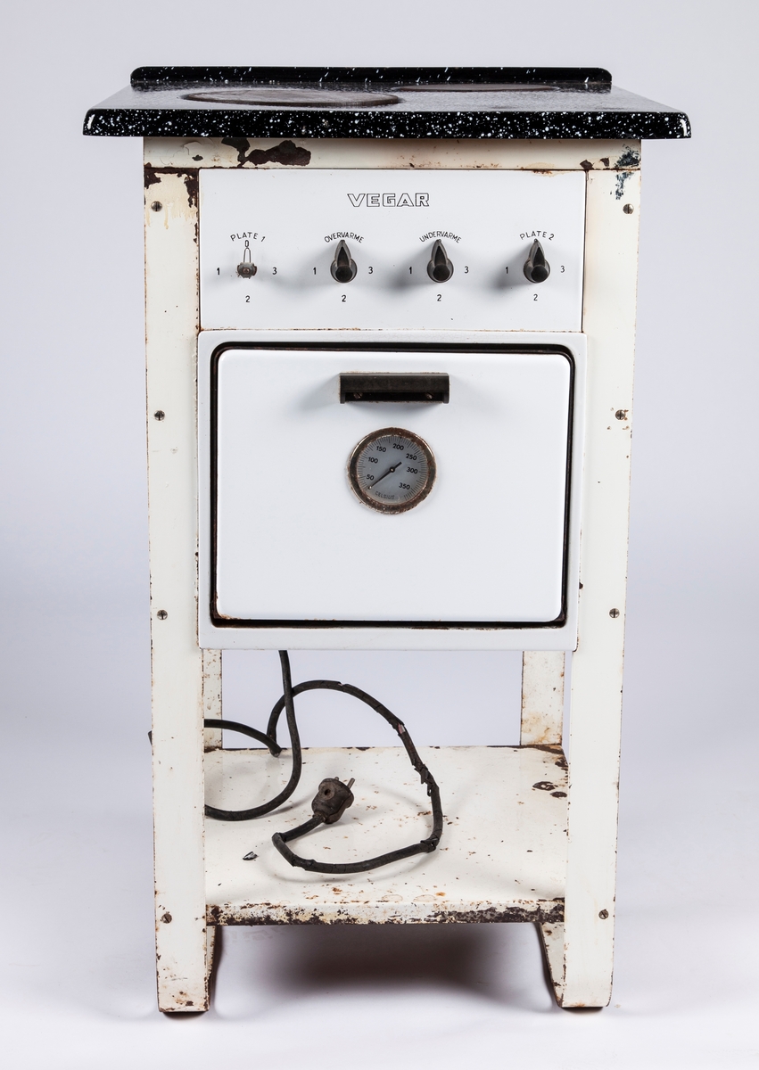 FHM.07891a: Elektrisk komfyr, kvadratisk, to kokeplater,  4 ben.
Hylle under stekeovn.
FHM.07891b: Stekeovnrist, 27x29,5 cm.