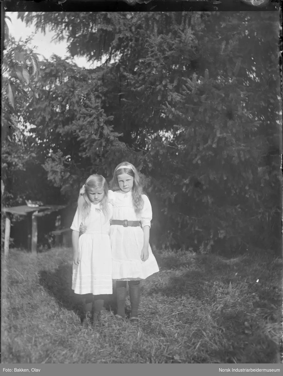 To jenter stående oppstilt i kjole utendørs.