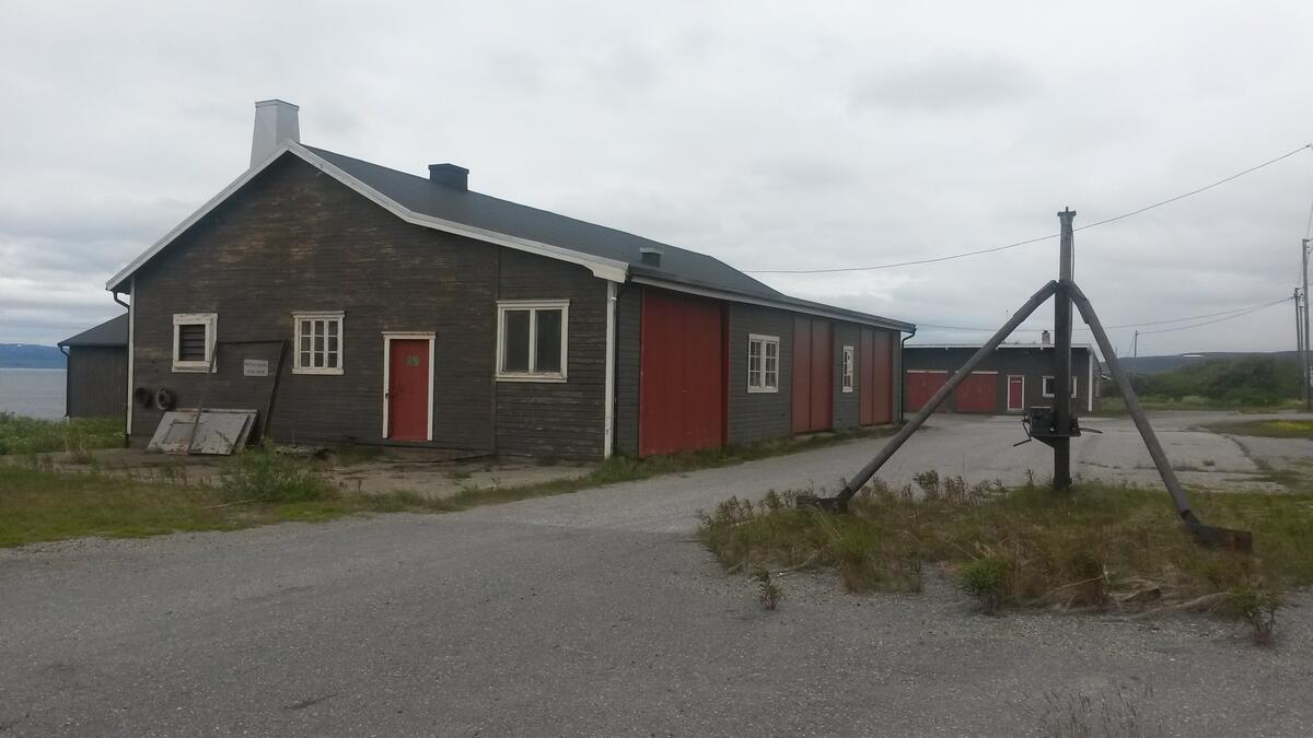 Smia på Vegsletta i Vadsø før oppussing. Brun bygning med røde dører og hvite karmer rundt vinduer.