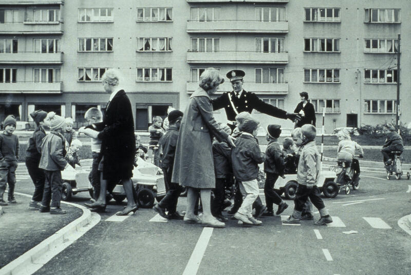 Fotografi at en gruppe barn og voksne som krysser vei med hjelp fra en betjent.
