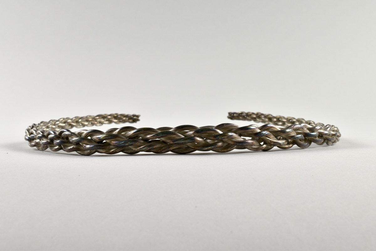 Öppen, stel, halsring av silver från vikingatid.
Tillverkad av åtta tjockare silvertrådar som är sammanflätade. Halsringen är tjockare på mitten och smalnar av mot ändarna.