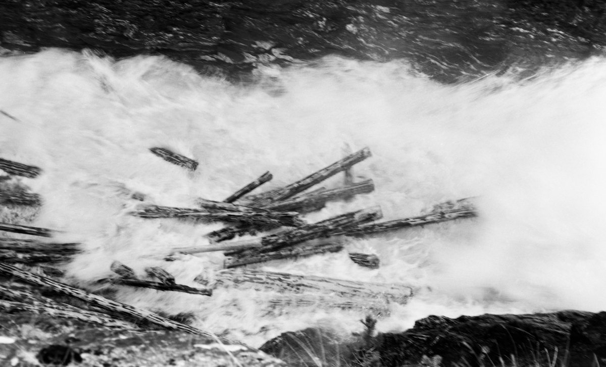 Tømmervase i elva Vinstra i Nord-Fron kommune i Midt-Gudbrandsdalen. Fotografiet er tatt i e trang, berglendt del elveløpet, nedenfor elvas utløp fra innsjøen Olstappen og kraftverket ved Kamfossen våren 1963. Tømmeret var barket.