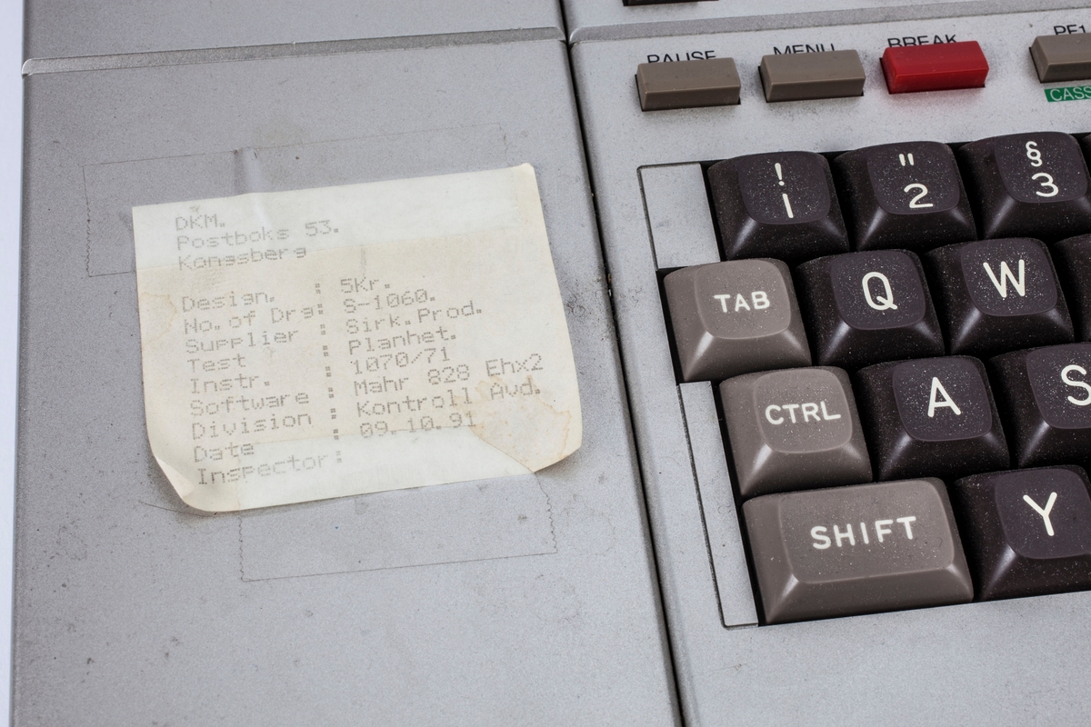 En bærbar datamaskin med en liten skjerm, tastatur, spiller for mikrokassett og innebygd miniprinter. Det ligger en kastett i spilleren.