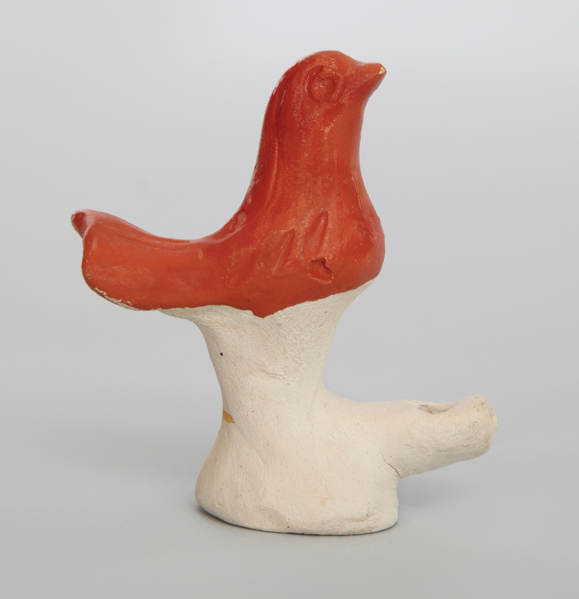 Spaltefløyte i keramikk i form av en liten fugl på en sokkel. Fuglen orange glasert, selve sokkelen uglasert.
Spalte og labium i sokkelen.
Ingen fingerhull.
