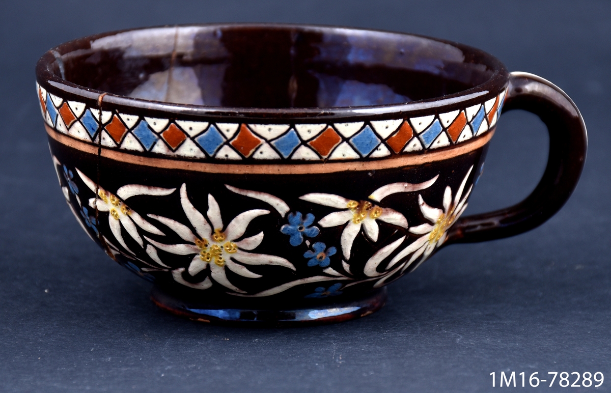 Kaffekopp i lergods med detaljerad målad och ristad dekor föreställande blommor, bland annat edelweiss och förgätmigej. Tillverkare är manufaktur Josef Wanzenried, verksam i kommunen Steffisburg i distriktet Thoune i Schweiz.