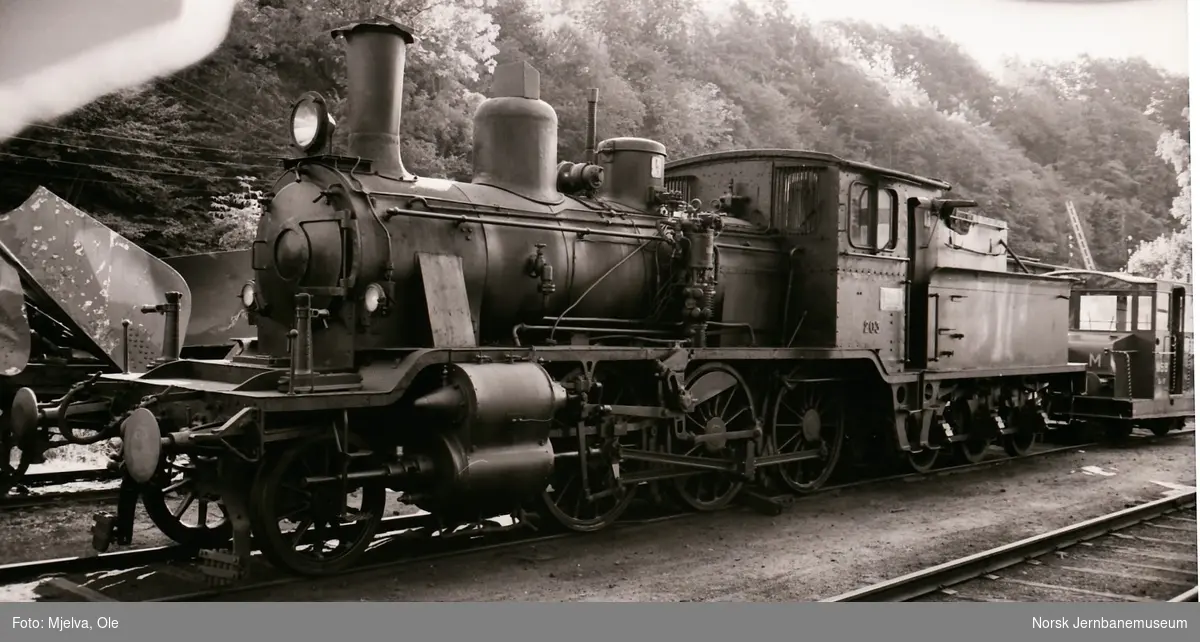 Hensatt damplokomotiv type 21e nr. 203 på Arendal stasjon. Til høyre skiftetraktor litra Skb 202 17
