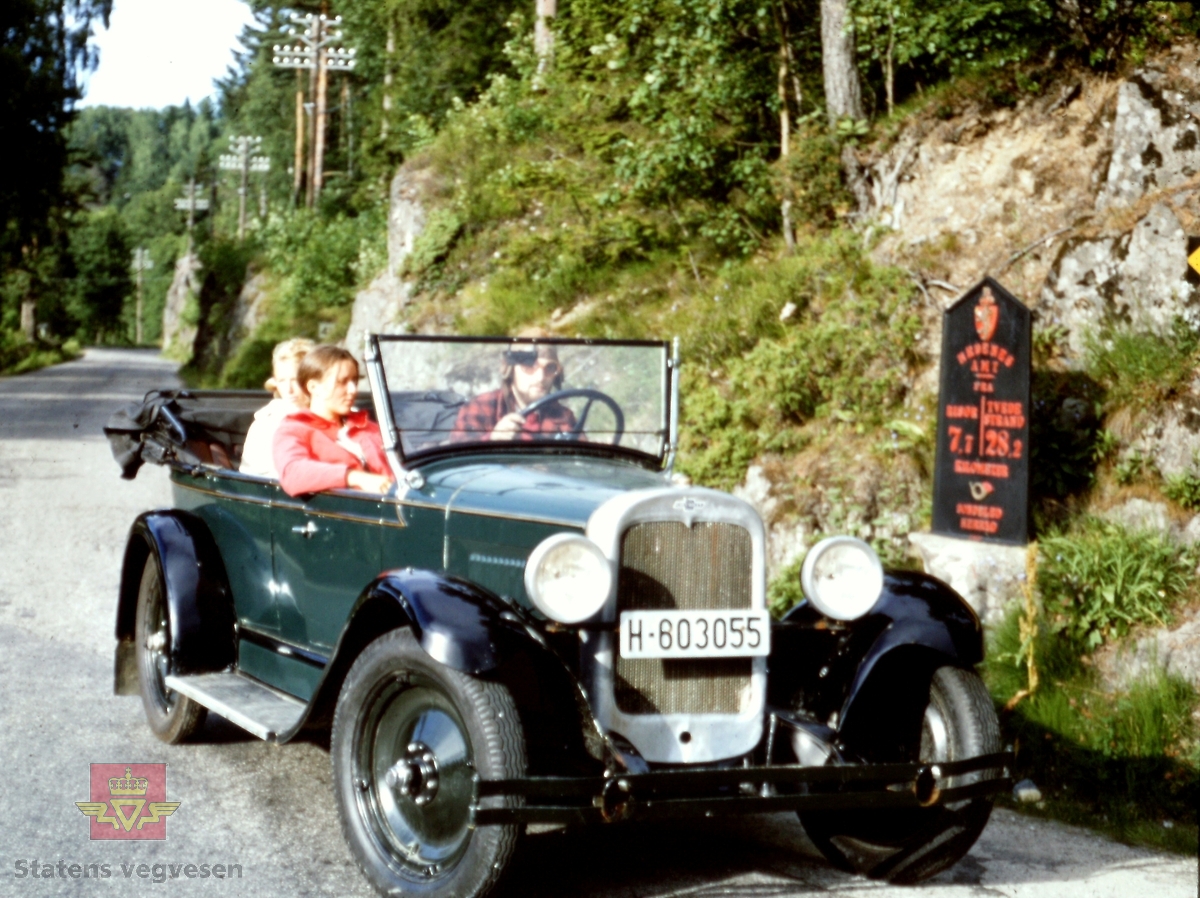 Bilen er en 1927 modell Chevrolet Touring som tilhører Erik Holand fra Tromøya. 
Bildet er tatt i Bossvik i Risør. Risørvegen, Arendal. 
Tekst på milepæl: Riksvåpen med løve og krone + posthorn. Tekst: NEDENES AMT FRA RISØR 7,7-TVEDESTRAND 28,2 KILOMETER. ARENDAL HERRAD. Denne er i dag lagret på Statens vegvesens samlinger på Labro, Kongsberg.
