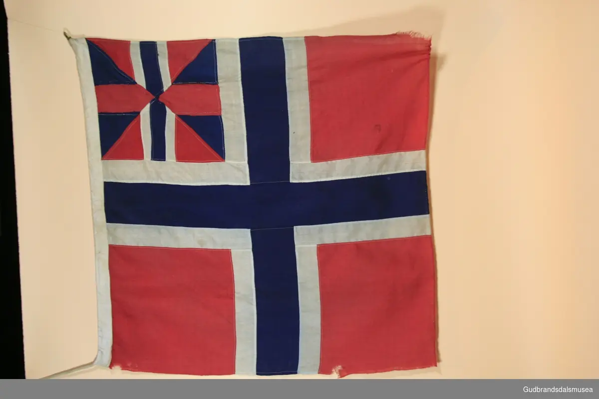 Norsk flagg med innfelt engelsk flagg. I en kanalgang til venstre er det sydd inn en trestang og en flettet snor som festeanordning. Det engelske flagget er sydd inn øverst til venstre.