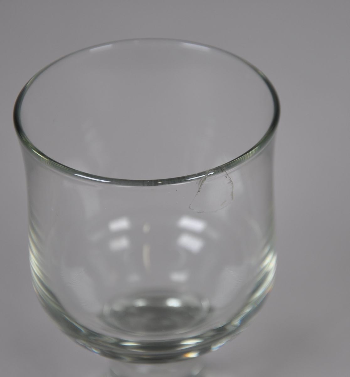 Grått hetvinsglass. Glasset står på sylindrisk stett og rund sokkel. Glasset er sylindrisk, med svak konkav kurve under drikkeranden. Det er sprekkdannelse ved drikkeranden.