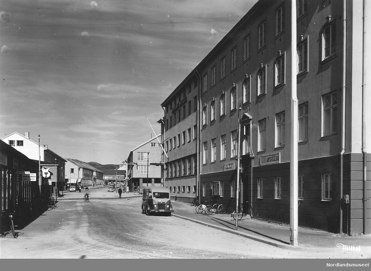 Oppover Storgata, Bodø, fra administrasjonsbygget til Saltens Damp. Noen biler og mennesker.