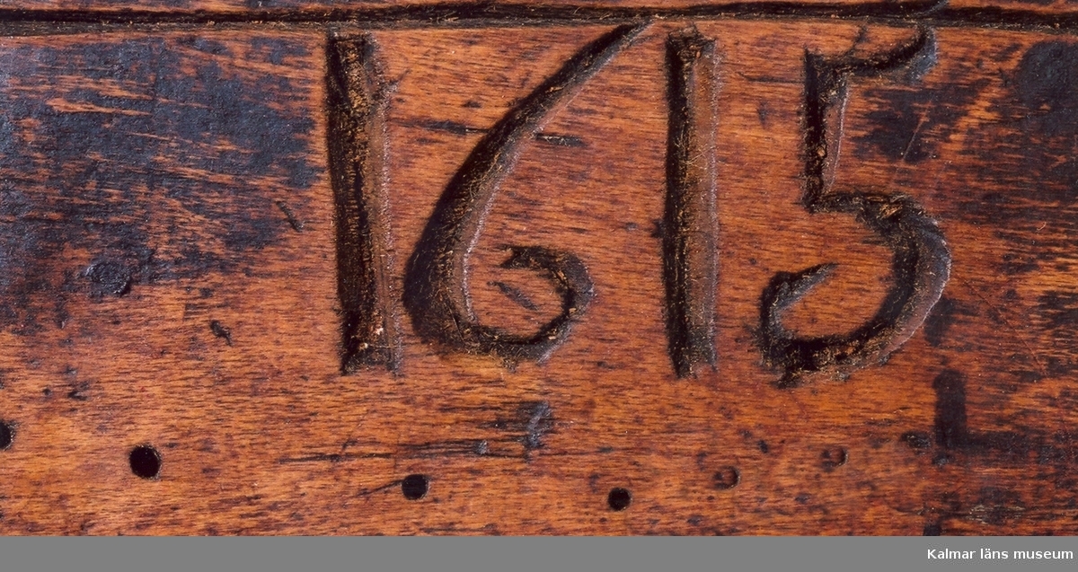 KLM 2100. Låda av trä. Fyrkantig, skjutlock med grova ornament. Skuren i ett stycke. På ena sidan: 1615, på den andra E.L. På locket inristat en månguddig stjärna. Okänd användning.