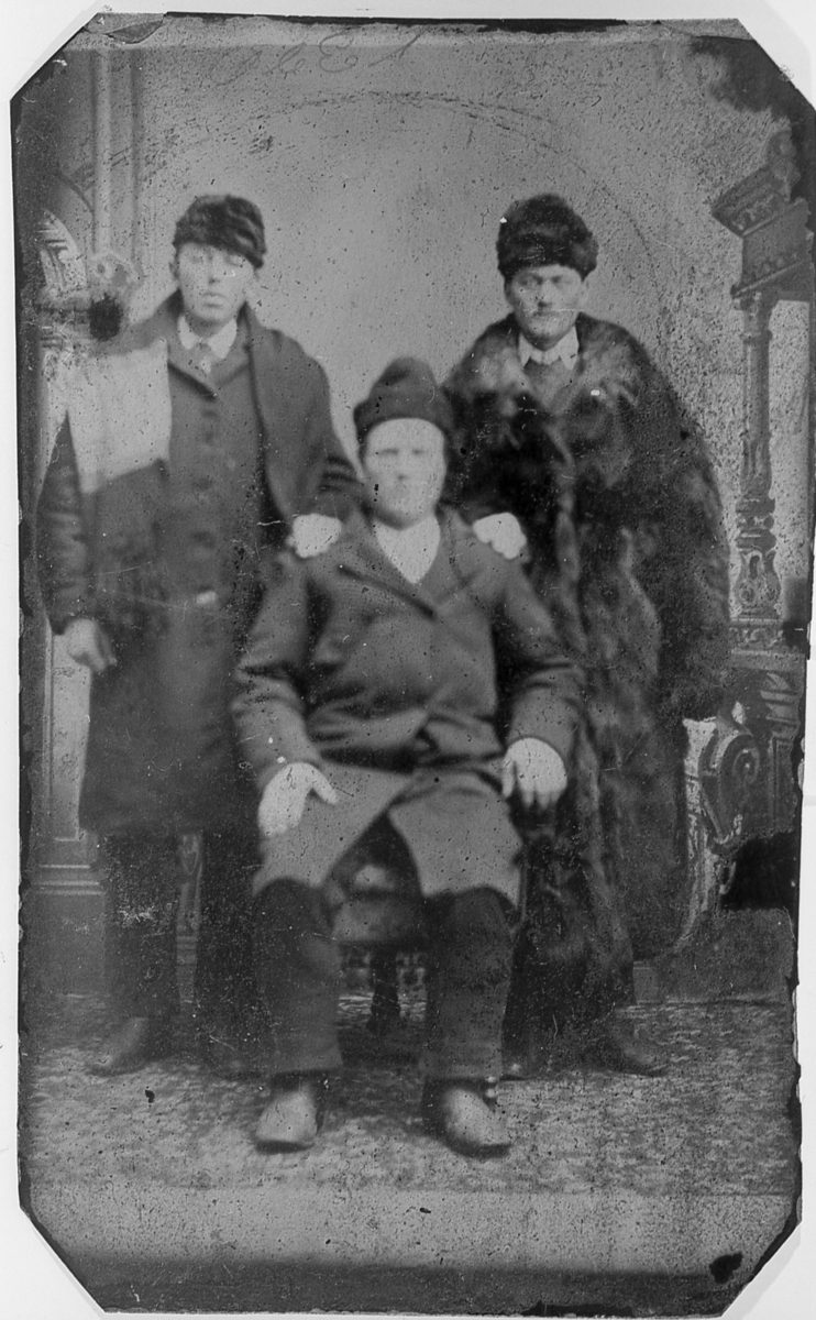 Atelierfotografi av tre uidentifiserte, vinterkledde menn. Muligens utvandrere i USA.