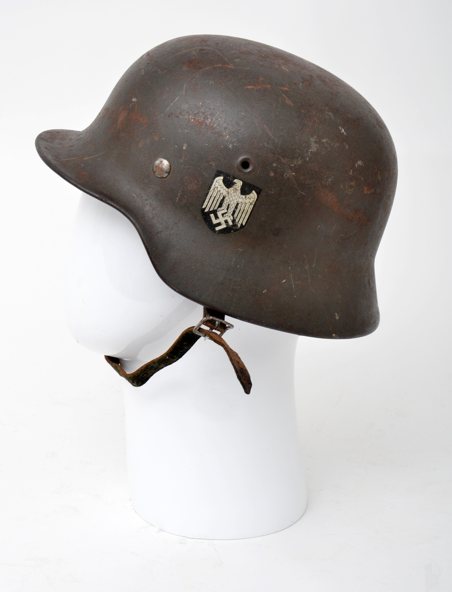 Militærhjelm i stål med regulerbar polstring i skinn og lærreim. På venstre side av hjelmen er et merke i sølv og sort av den tyske ørn og hakekorset.