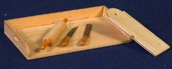 Bakbord med skärbräda, kavel, kniv och spatel. Bakbord av omålat trä med tre låga kanter med utsågade handtag på båda kortsidorna. Märkt "Nolbyn" på undersidan. Skärbräda av omålat trä, rektangulär form med rundad ovansida med hål för upphängning. Mått: L 45 mm, B 16 mm. Brödkavel av omålat trä. Slät kaveldel med rundat handtag i båda kortändar. Mått: L 45 mm, D 6 mm. Kniv med omålat trähandtag och blad av metall. Vass egg. Mått: L 32 mm, B 3 mm. Spatel med omålat trähandtag och spatelblad av metall. Mått: L 33 mm, B 3 mm.