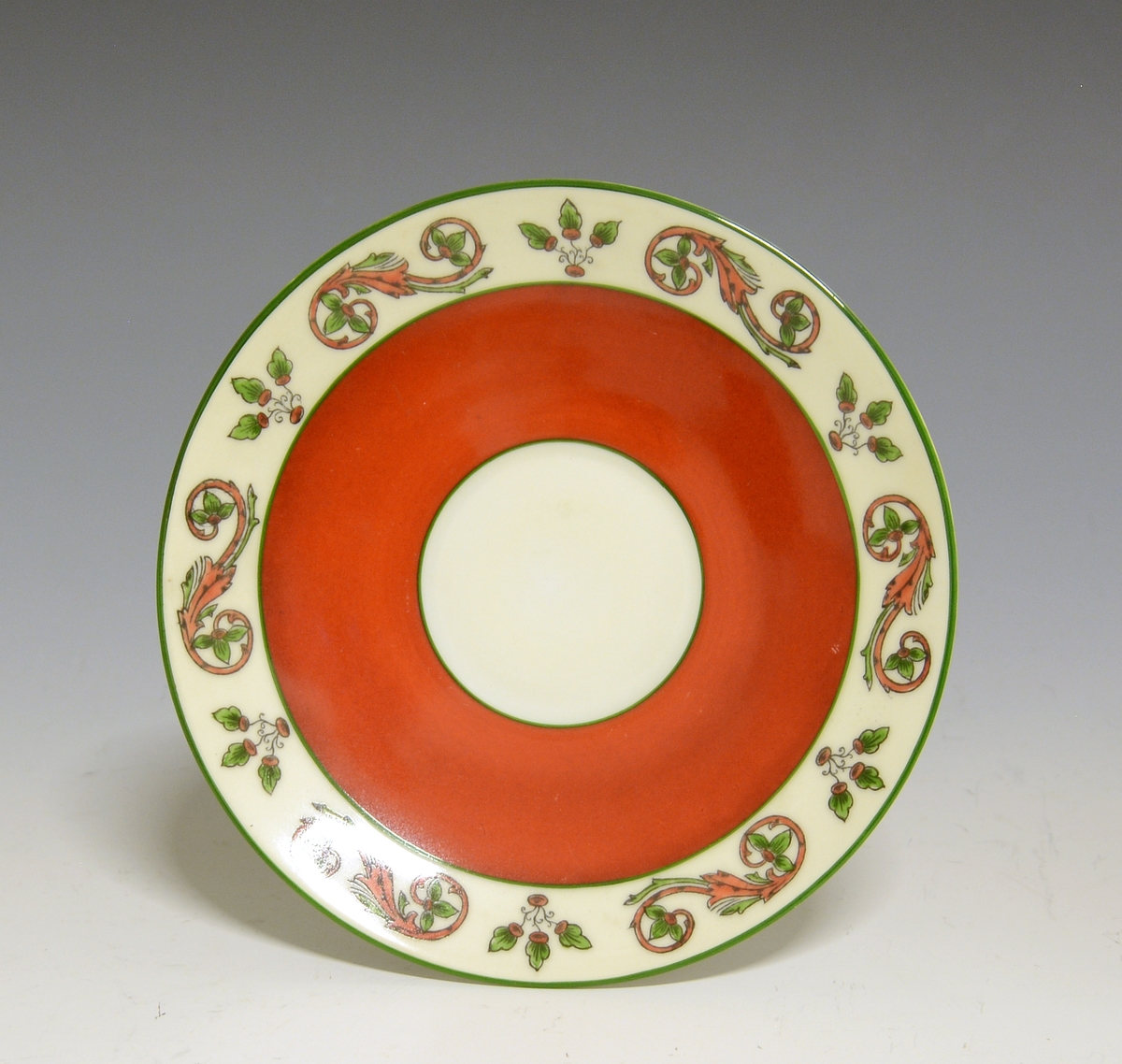 Prot: Skål av porselen. Hvit glasur under. Oppå malt rød med utsparing for kopprand og rand langs kanten som er "rosemalt" i rødt og grønt.
