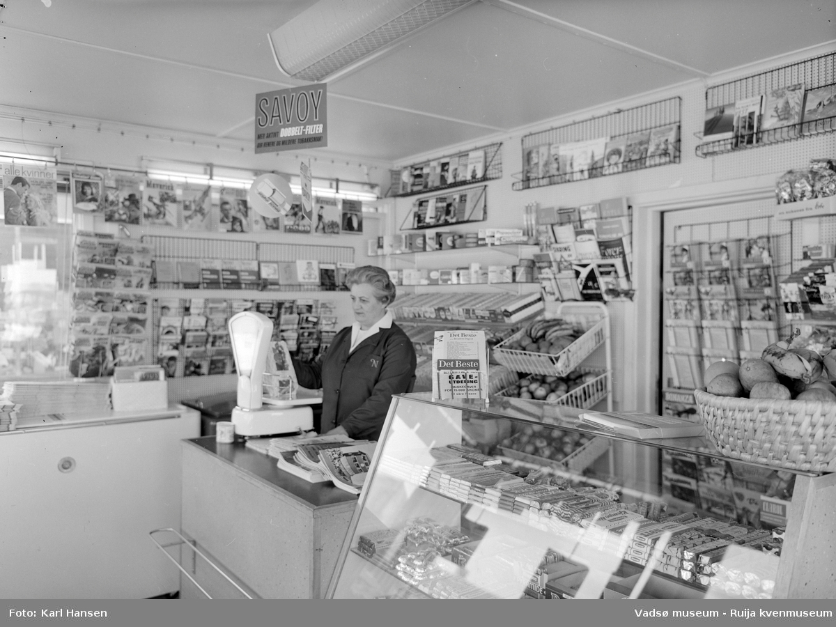 Narvesen kiosk, Vadsø 13.mai 1965. Deler av interiøret og vareutvalget i kiosken. Kioskansatt Anny Iversen.