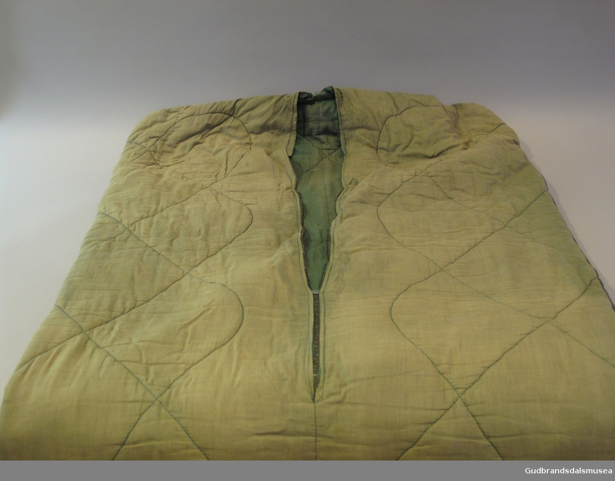 Tynn grønn sovepose i vattert bomull og med vanntett stoff på undersiden. Glidelås i øverste del av soveposen.