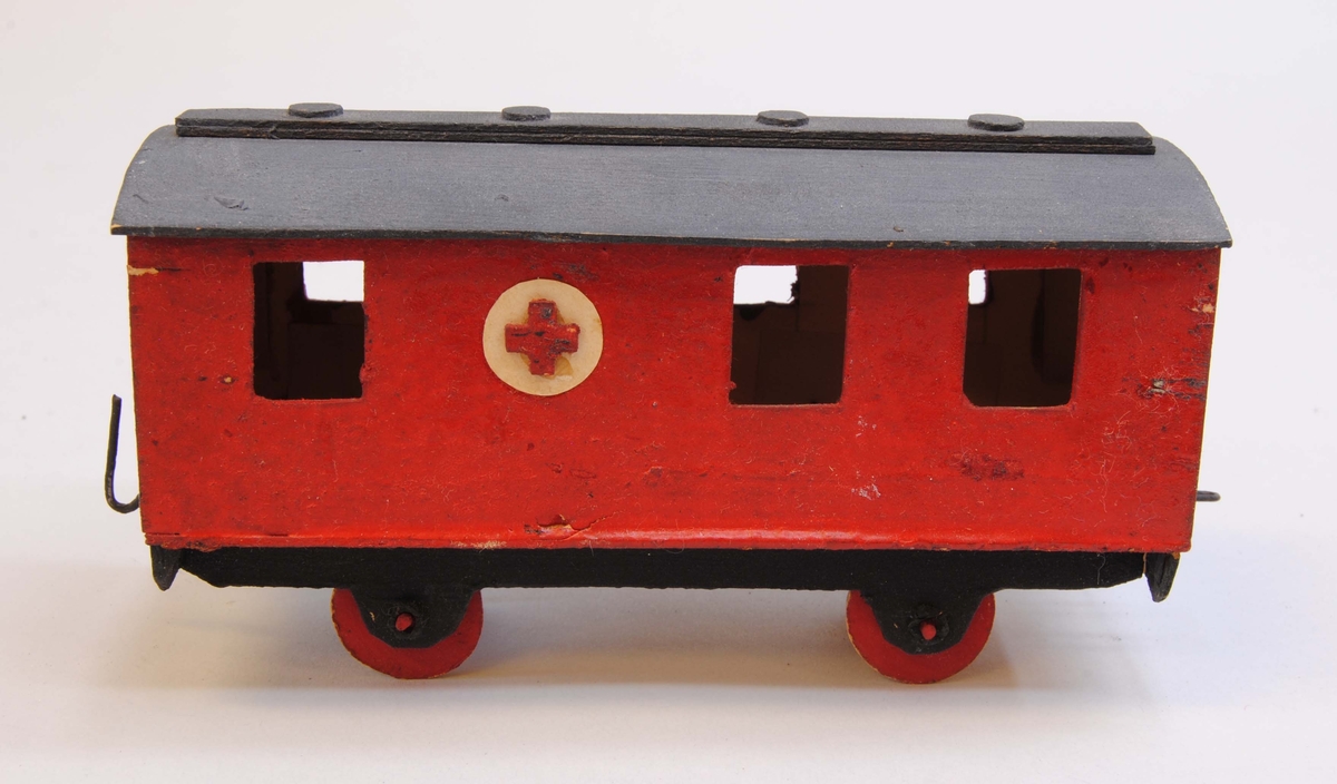 Röd sjuktransportvagn av papp med en vit cirkel med ett rött kors på var sida.
Delarna är limmade eller sammanfogade med rött lack. Hjulen är gjorda av papp och hjulaxlarna av fyrkantiga träpinnar, troligtvis tändstickor. Vagnen är målad röd med mörkgrått tak, svart underrede och röda hjul. Under vagnen är datumet "30/3 1919" handskrivet.
På kortsidorna av vagnen finns böjd ståltråd, en ögla och en krok, för att koppla samman vagnen med andra vagnar eller lok. Vagnen har ett välvt tak med en avlång rektangel i mitten med fyra runda upphöjningar som föreställer lamphuvar och tre fönster på varje sida av vagnskorgen.