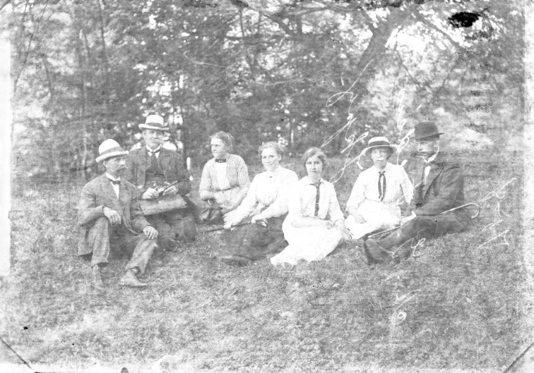 Tre män och fyra kvinnor sitter på en grässlänt.