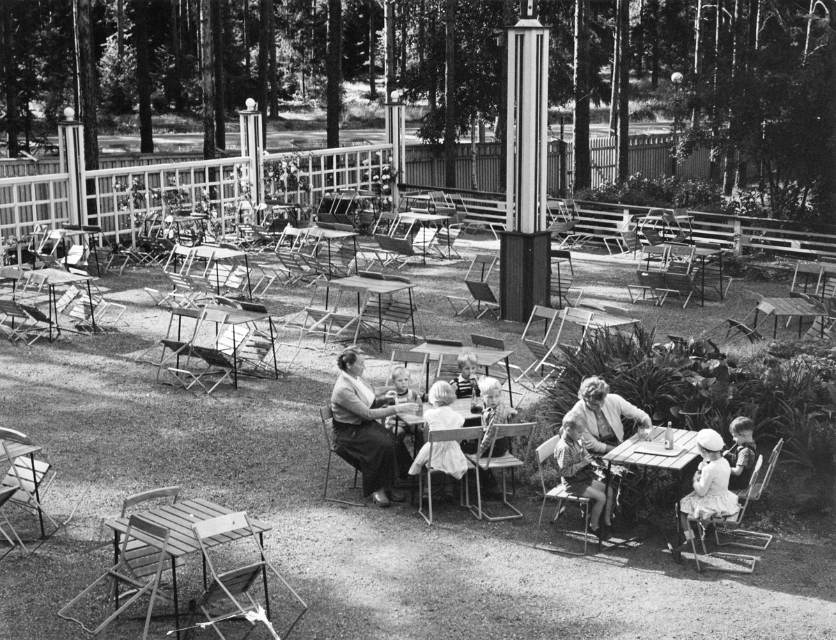 Uteservering i Folkets Park i Linköping. 1950-60-tal. Vid två av borden sitter barn och en kvinna vid varje bord.