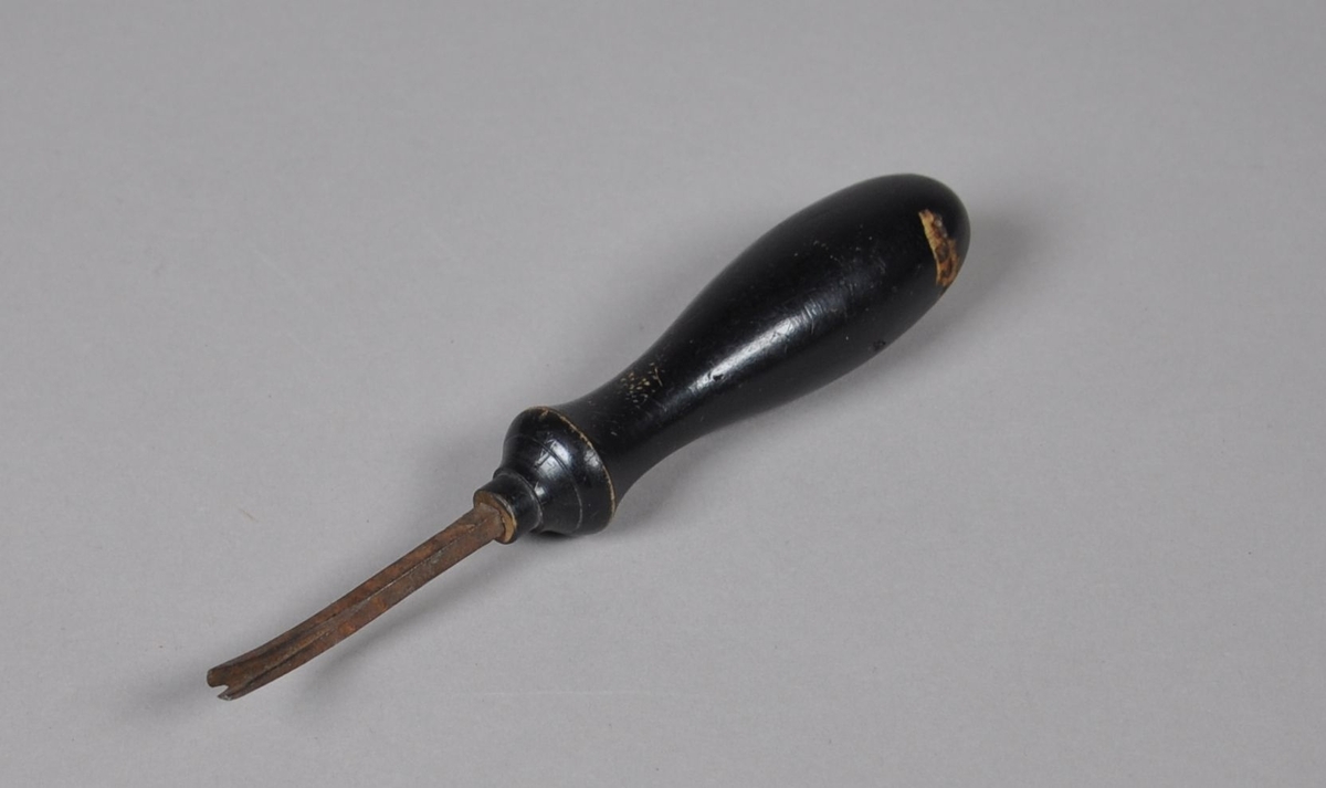 Beiskniv av jern, med dreid eller svarvet håndtak av tre. Jernet har buet form og splittet spiss. Håndtaket er malt svart.