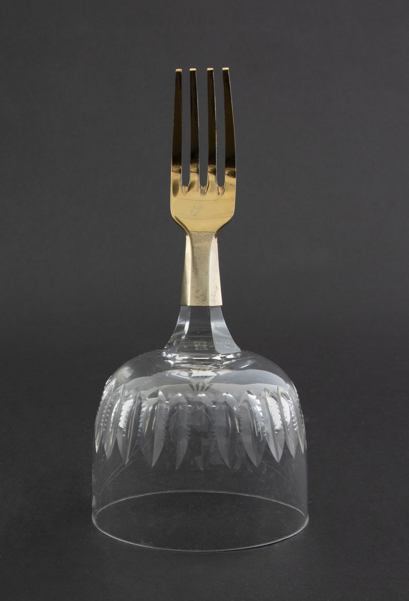 Objektet består av en halv forgylt gaffel som er montert på et vinglass med lansettformede slipninger.