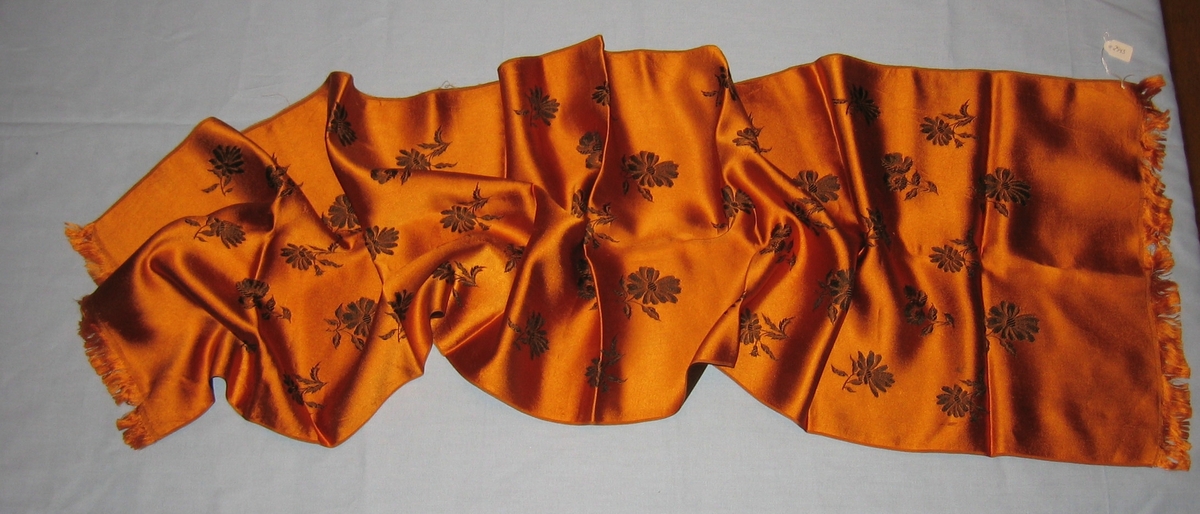 Oransjegyllent, glatt stoff med mørkebrun, maskinbrodert blomsterdekor.
