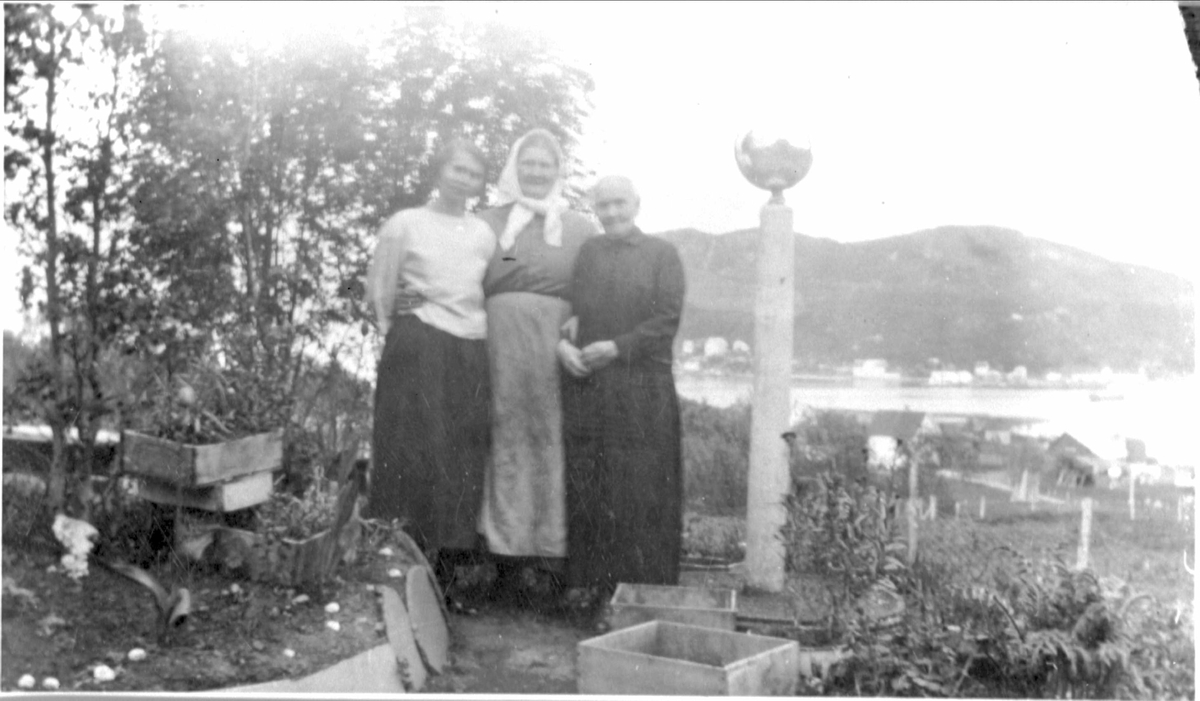 Amatørportrett av to eldre og en ung kvinne stående i hage.